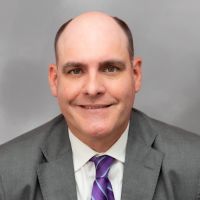 T. Wayne Williams in a suit with shoulder-length hair and a patterned tie, smiling in a portrait