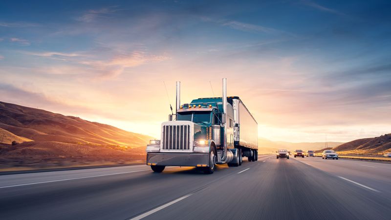 Powerful semi-truck driving on highway at sunset, with scenic mountains in the background.