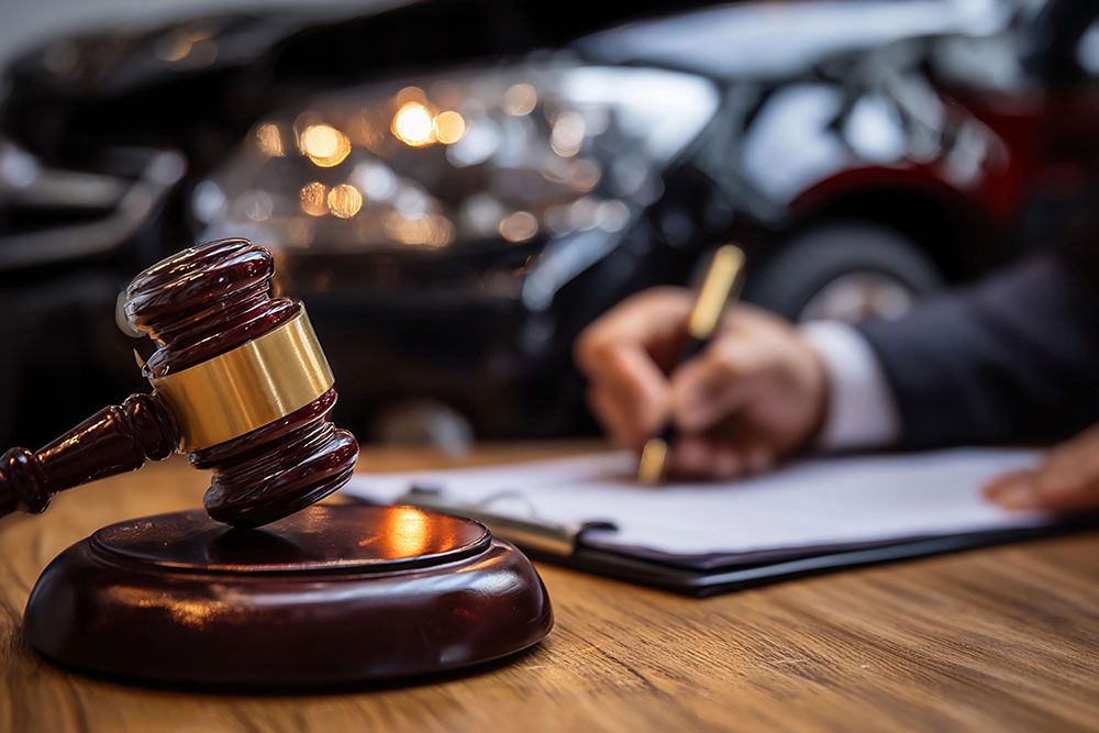 Gavel on table with person writing, car accident background. Legal steps after auto collision.