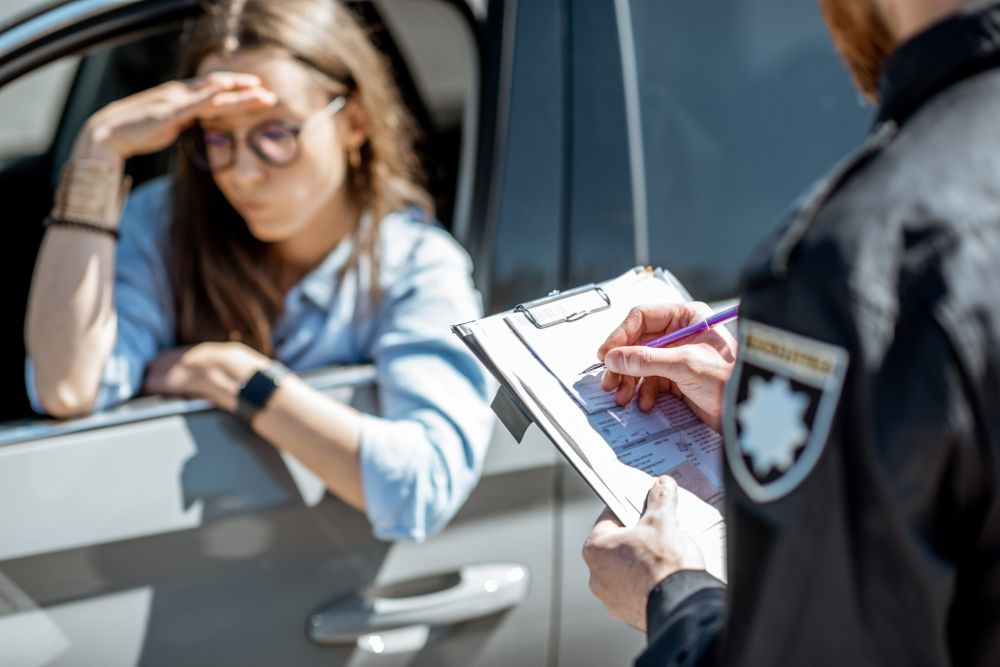 Female driver looking stressed as police officer writes a speeding ticket outside her car window