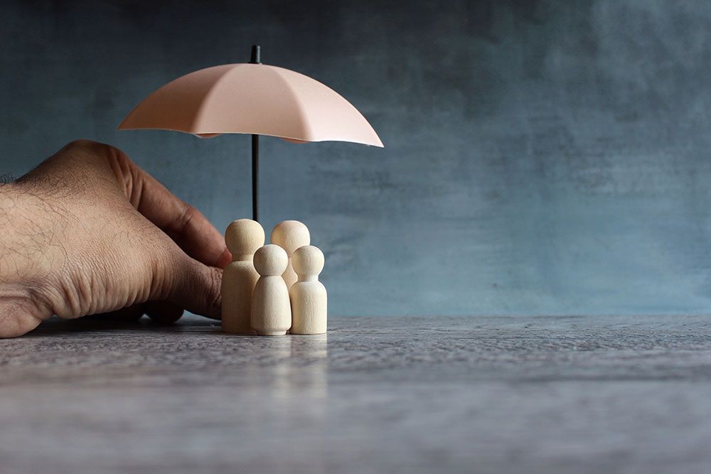 Hand holding umbrella over wooden family figures, symbolizing protection and security.