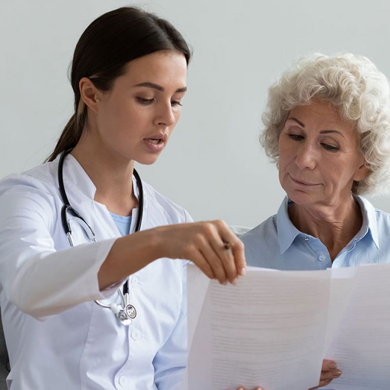 Doctor discussing medical documents with senior patient on a couch, highlighting attentive healthcare guidance.