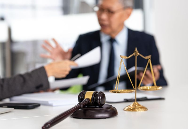 Gavel and scales on desk during legal discussion between professionals at a law office.