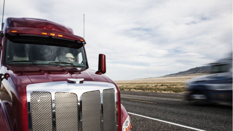 Two semi-trucks pass closely on rural highway, highlighting risk factors in a trucking accident