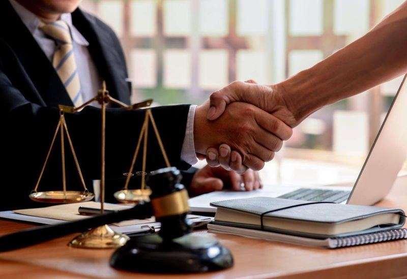 Handshake between lawyer and client at office desk with legal documents.