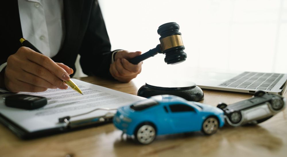 Abogado revisa documentos de casos de accidentes automovilísticos con un mazo y un auto de juguete, enfatizando su experiencia legal en reclamos de automóviles.