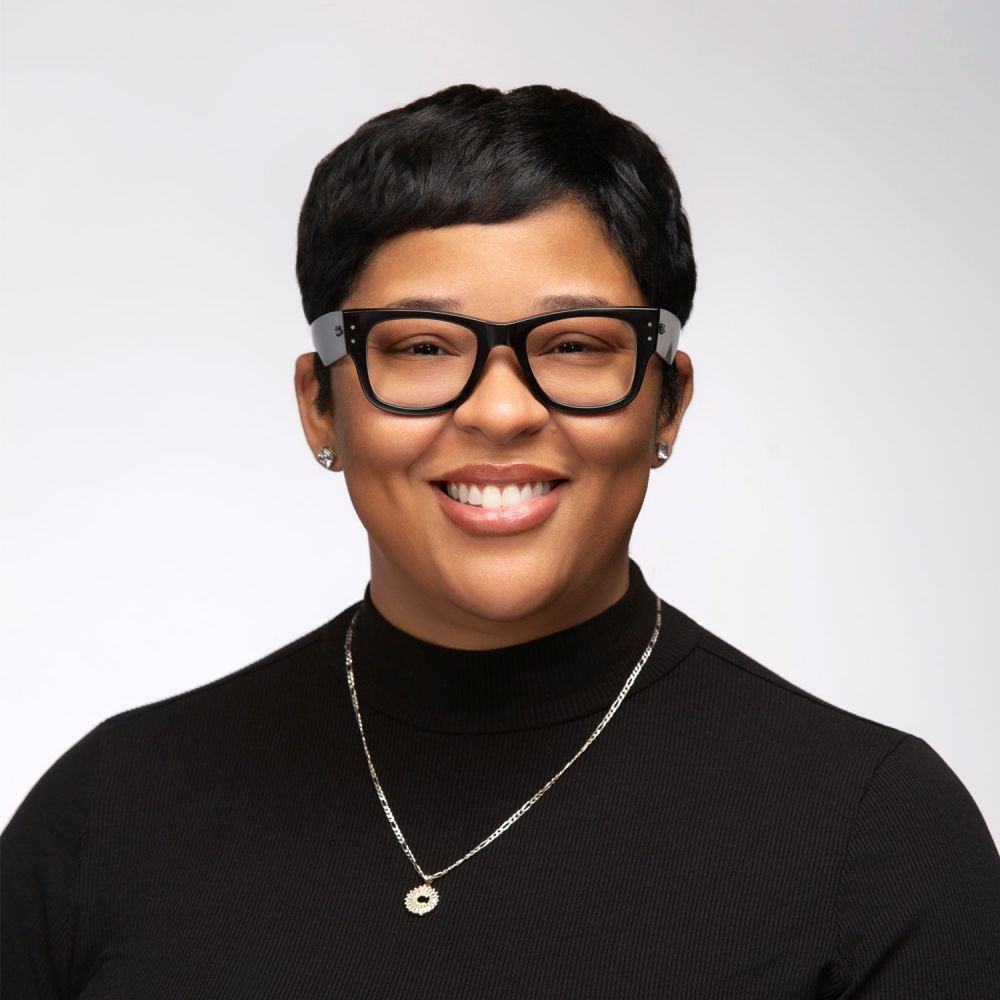 Charlene Ames in glasses, wearing a black turtleneck and necklace against a plain background.