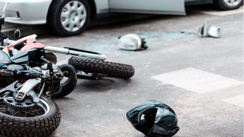 Motorcycle accident scene with a helmet on the road, near a car with damage.