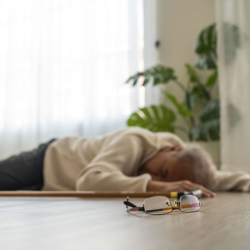 Elderly person fallen on floor with walking stick and glasses nearby, implying medical emergency or fall risk.