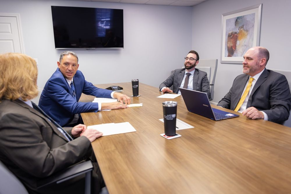Business meeting with four professionals in suits around a conference table, engaging in discussion.