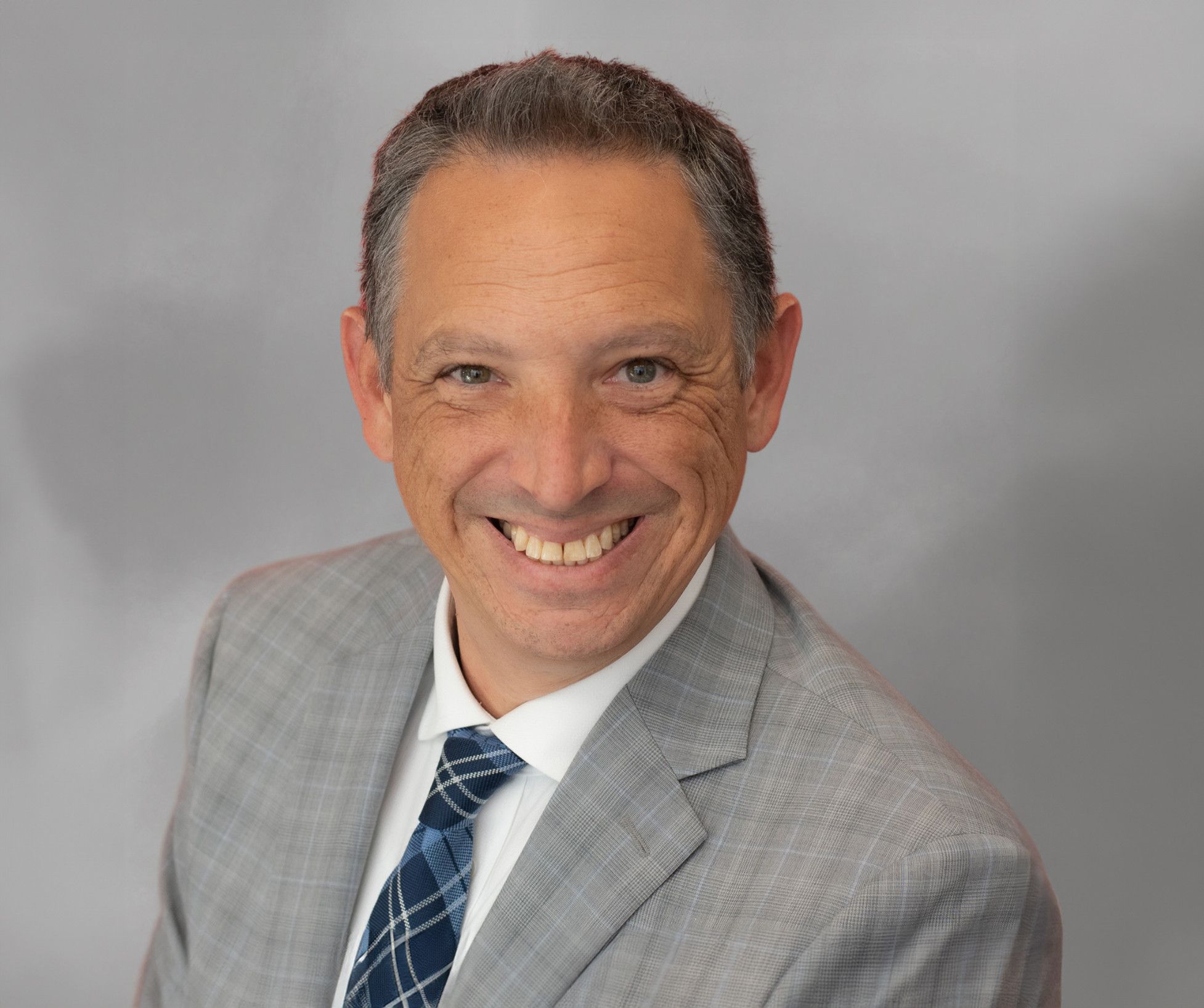 Smiling middle-aged man in a gray suit with a blue tie, professional portrait.