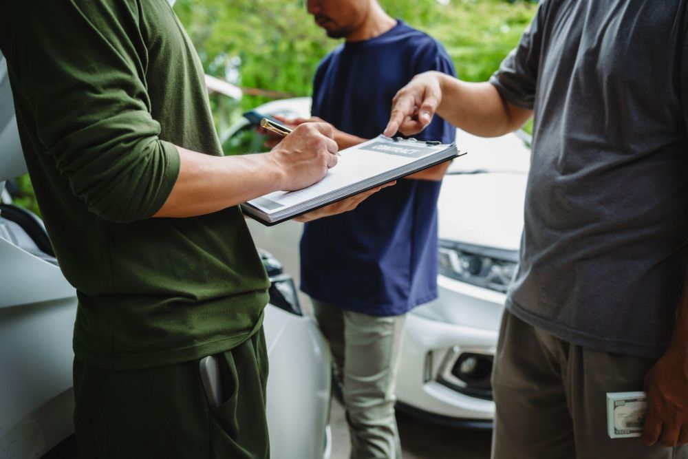 People signing a contract near a car, emphasizing agreement and negotiation dynamics in an outdoor setting.