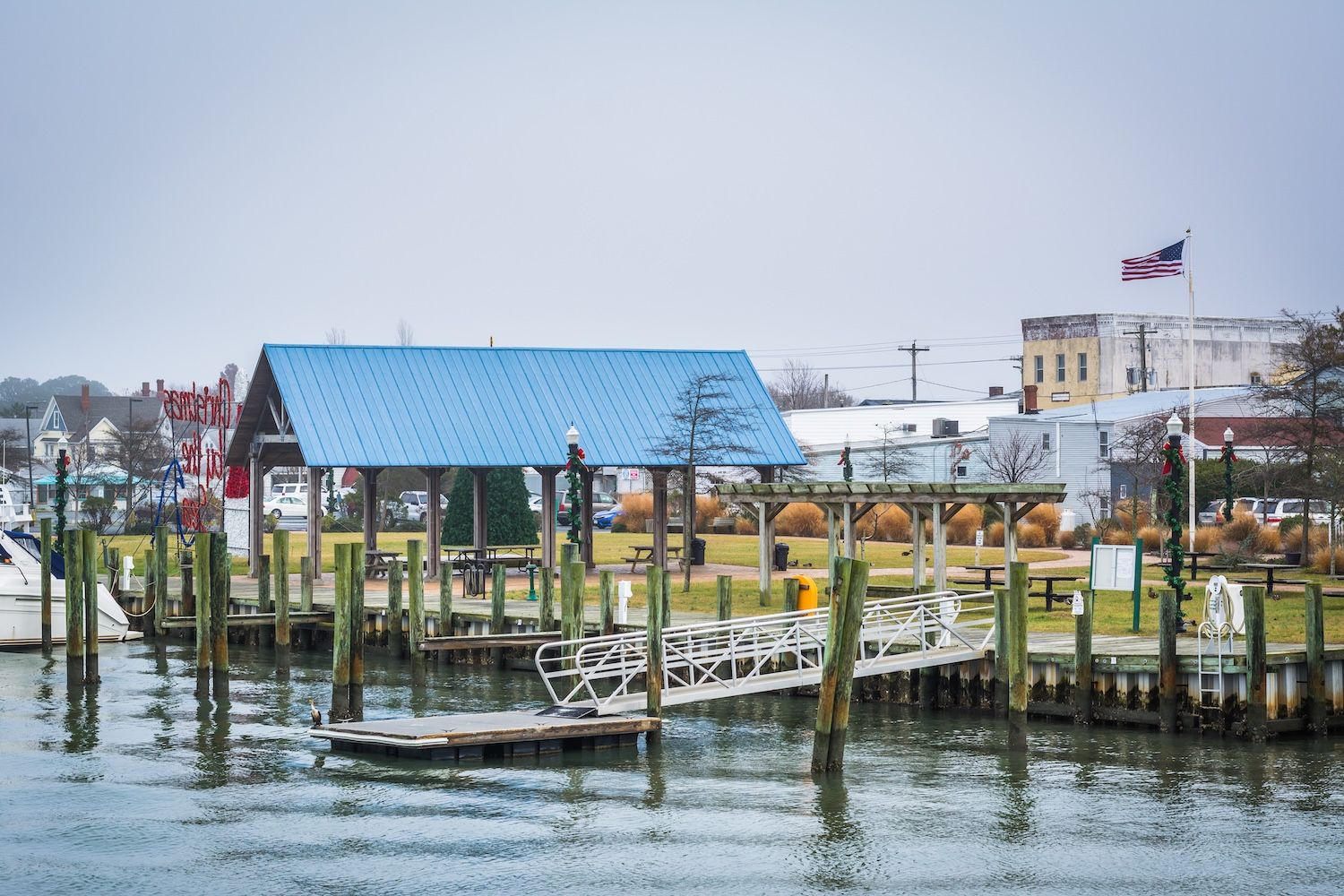 Harbor pier with blue-roofed building, American flag, and boats on a cloudy day.