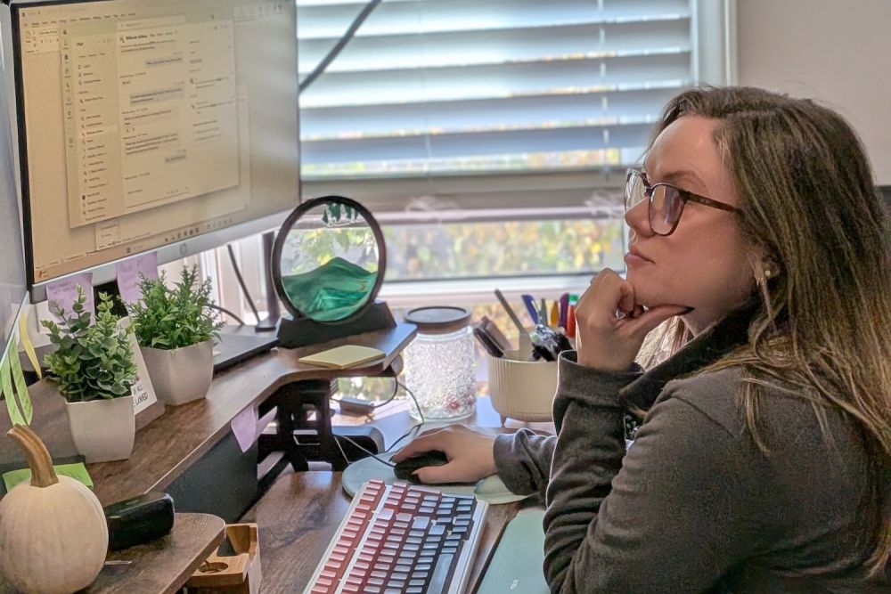 Woman working at a computer desk with plants, focusing on a task in a home office environment.