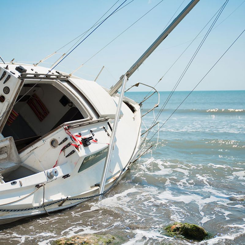 Sailing boat washed ashore, partially submerged in water under a clear blue sky at the beach.