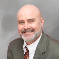 Attorney Robert Frazier wearing a suit and patterned tie against a gray background.