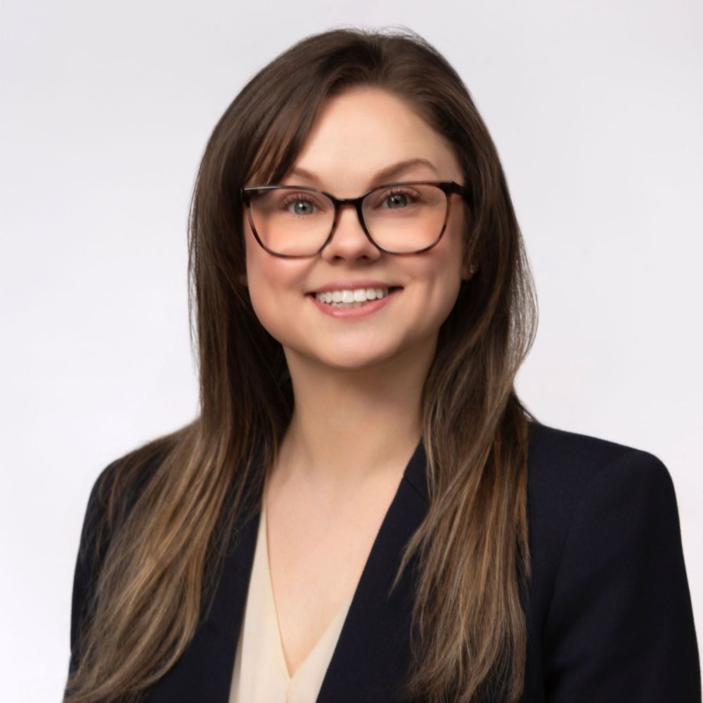 Kirsten Dunn smiling in business attire with glasses, long brown hair, on a white background.