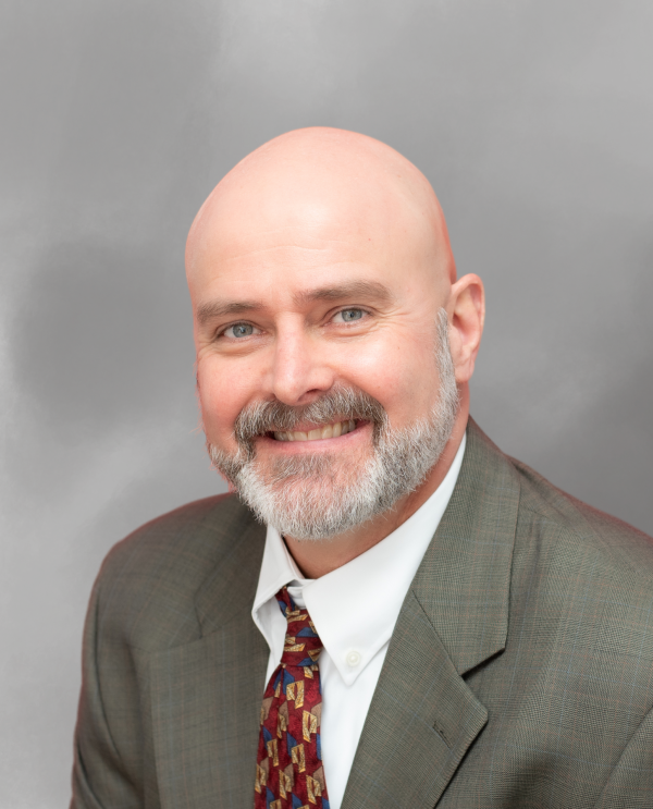 Attorney Robert Frazier wearing a suit and patterned tie against a gray background.