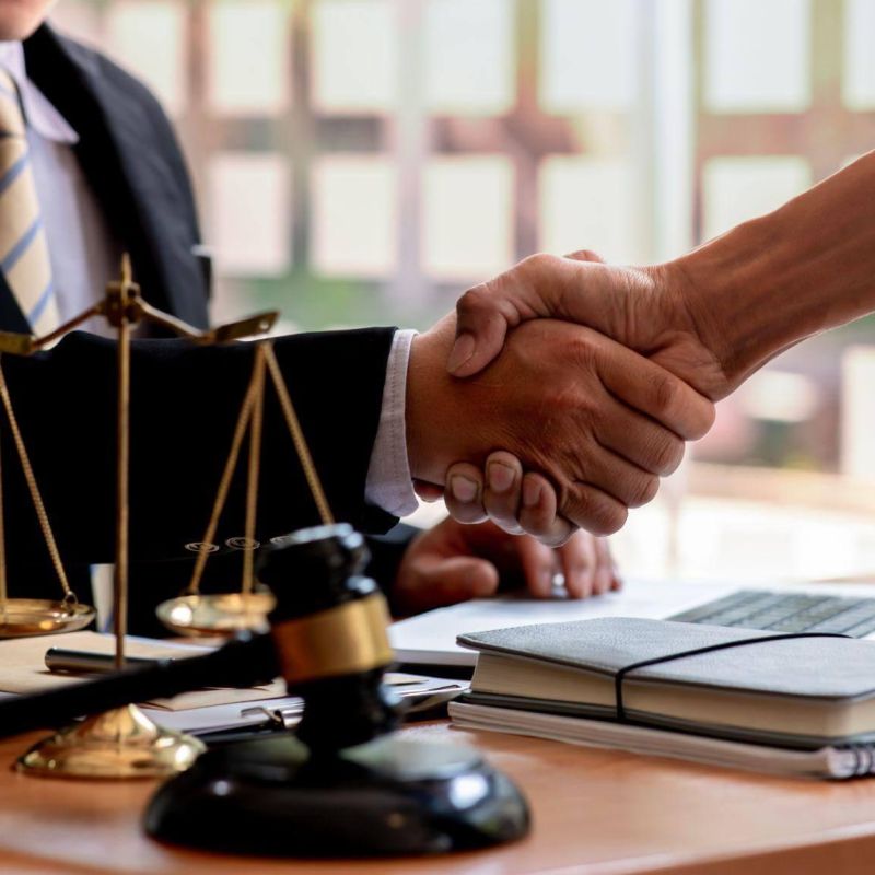 Handshake between lawyer and client at office desk with legal documents.