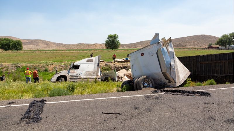Overturned semi-truck and damaged trailer off rural highway, aftermath of a trucking accident