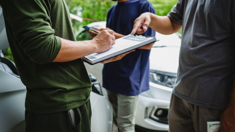 People signing a contract near a car, emphasizing agreement and negotiation dynamics in an outdoor setting.