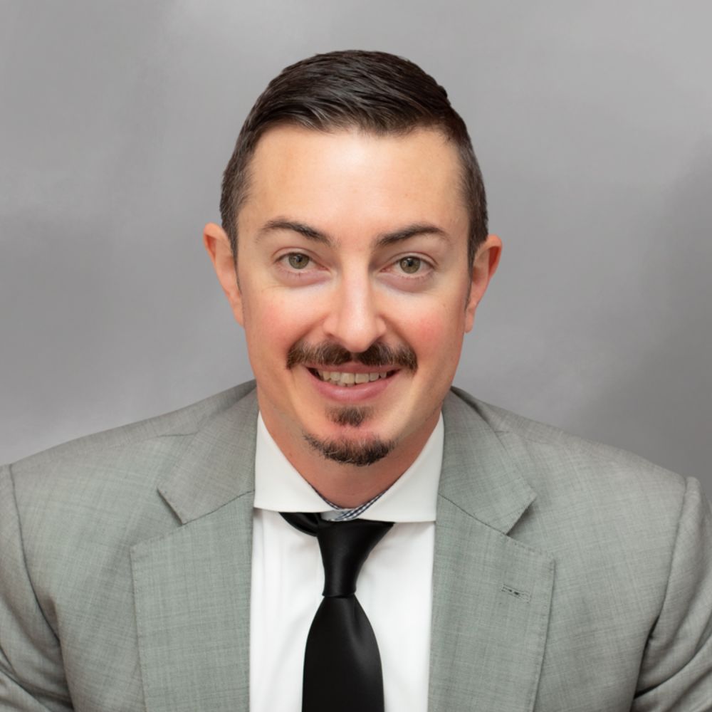 Andrew M. Coffarelli in a suit with shoulder-length hair and a patterned tie, smiling in a portrait