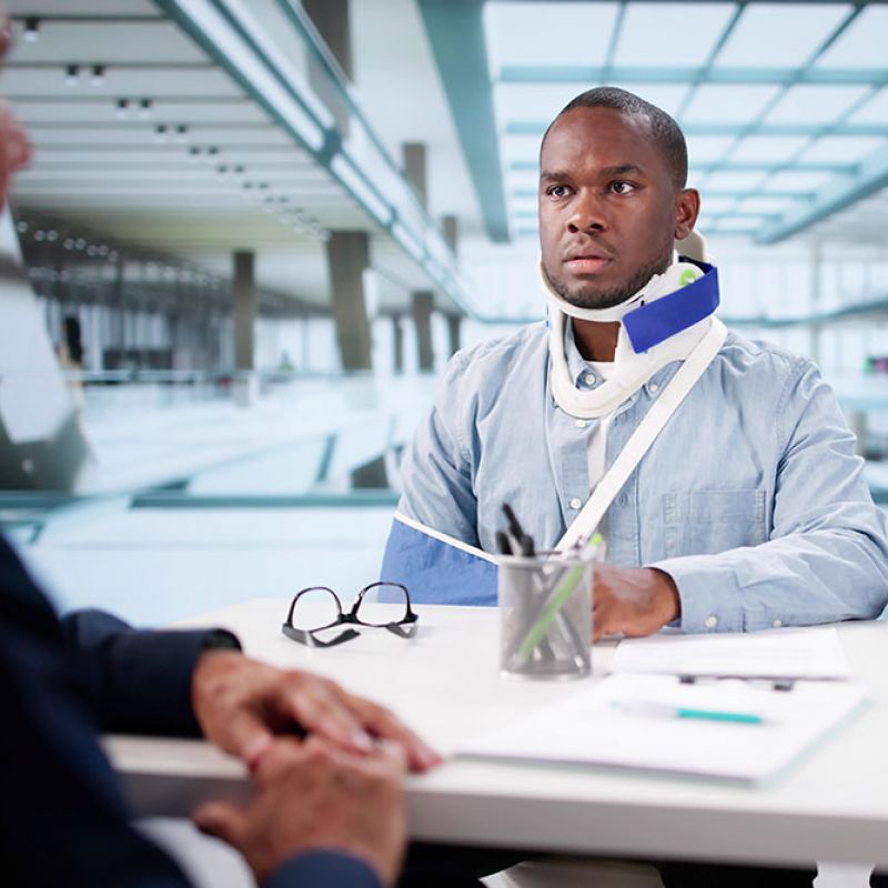 Man with neck brace and arm sling discussing with professionals in office setting.