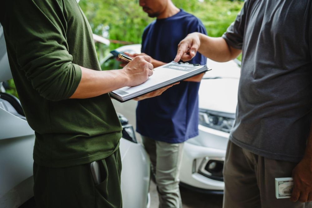 People signing a contract near a car, emphasizing agreement and negotiation dynamics in an outdoor setting.