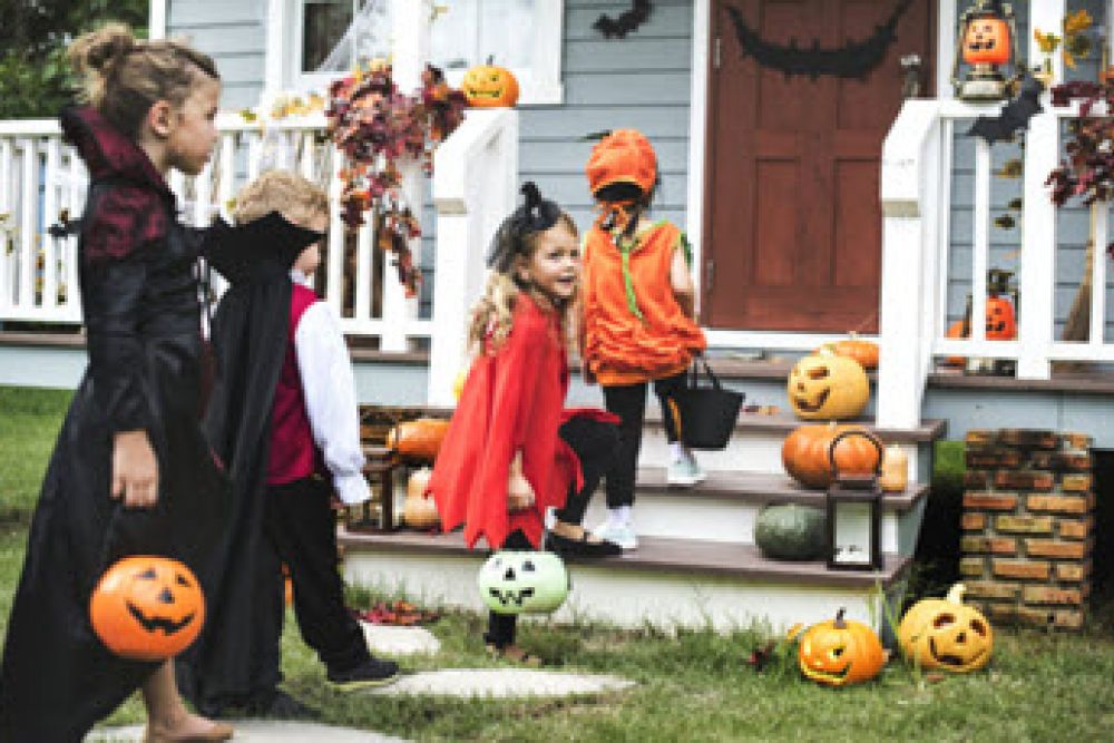 Children in Halloween costumes trick-or-treating at a decorated house with pumpkins and lanterns.