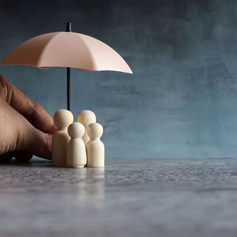 Hand holding umbrella over wooden family figures, symbolizing protection and security.