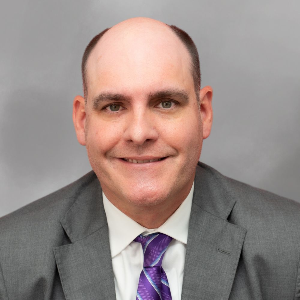 T. Wayne Williams in a suit with shoulder-length hair and a patterned tie, smiling in a portrait