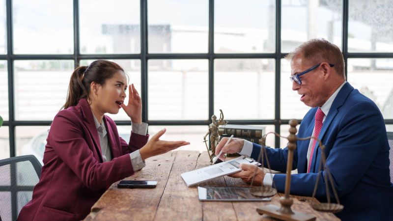 A businesswoman and lawyer discussing documents in a modern office setting with a tablet and scales of justice on the table.
