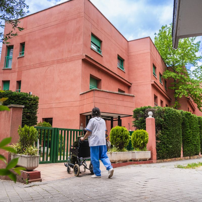 Caregiver pushing elderly resident in wheelchair outside nursing home; Williams DeLoatche handles nursing home abuse cases.