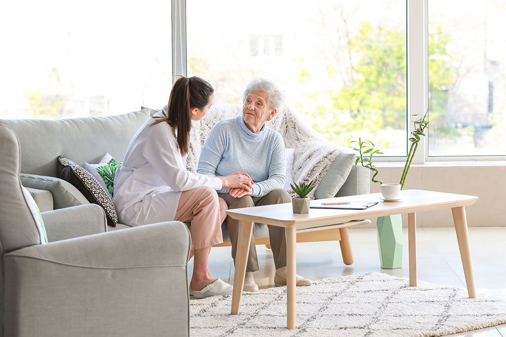 Caregiver and elderly woman sitting in a cozy living room, having a supportive conversation.