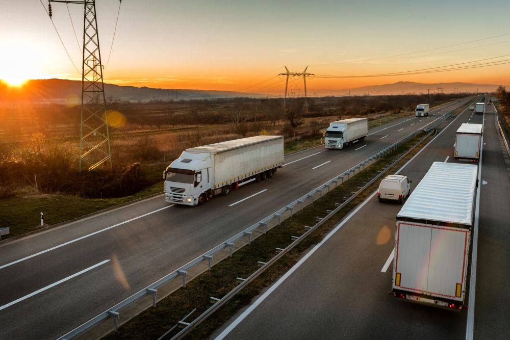 Convoys of White semi-trucks passing each other on a highway with a sunset and mountains in the background