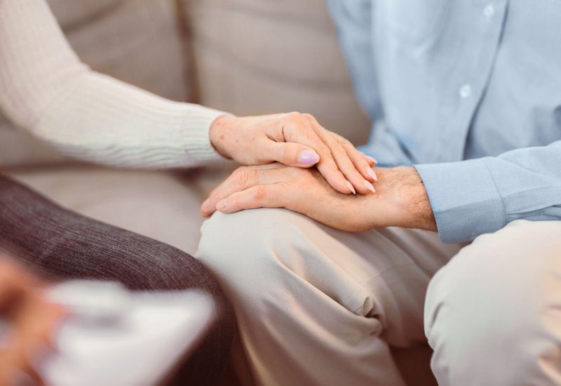 Two people holding hands, symbolizing comfort and support, with a focus on togetherness.
