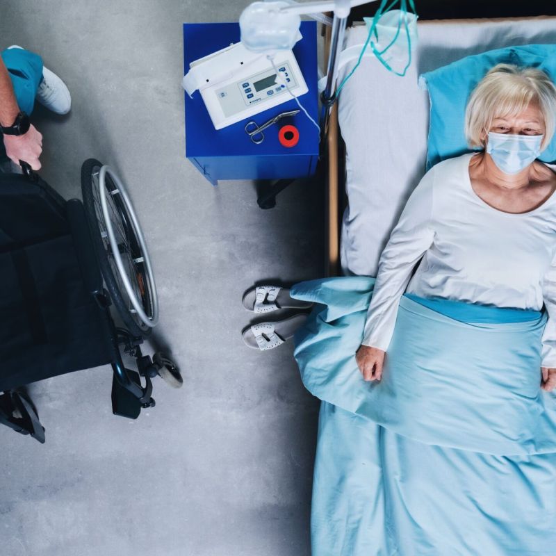 Vista aérea de un médico enmascarado que llega con una silla de ruedas junto a un anciano residente de un asilo de ancianos acostado en la cama