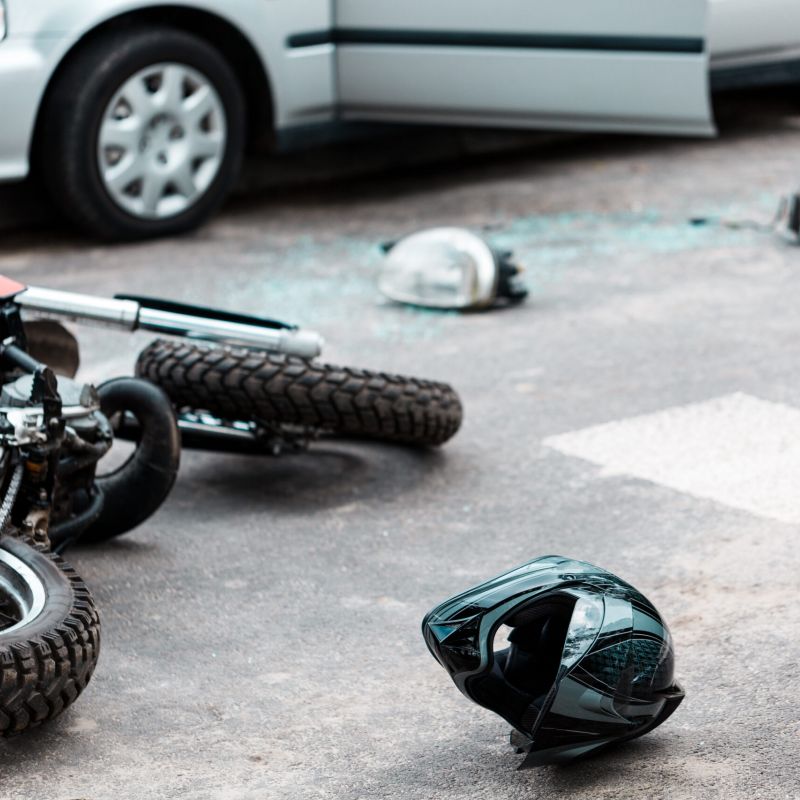 Motorcycle accident scene with a helmet on the road, near a car with damage.