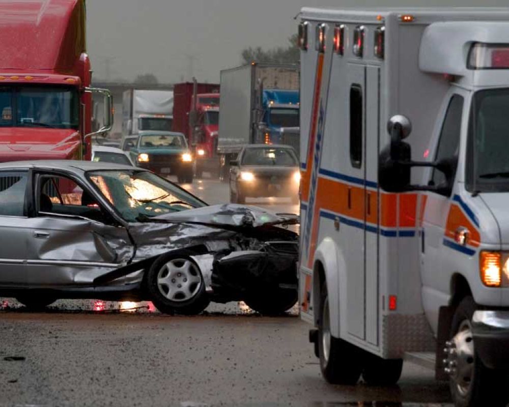Multivehicle accident involving car and truck with ambulance on rainy highway. Emergency response on scene.