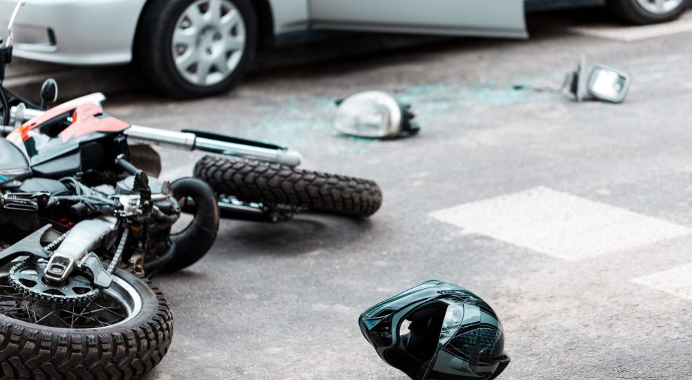 Motorcycle accident scene with a helmet on the road, near a car with damage.