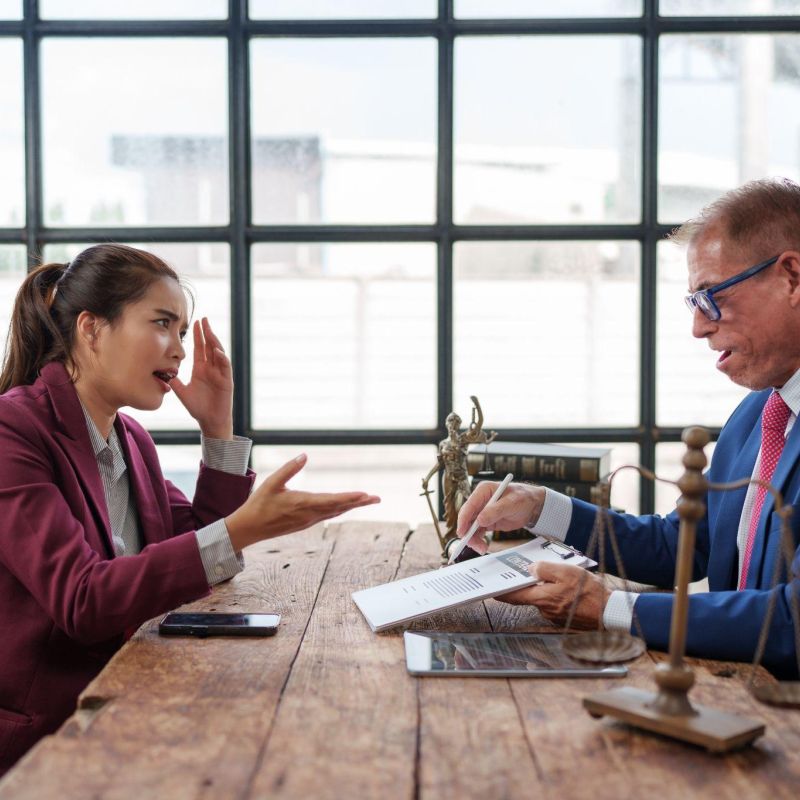 A businesswoman and lawyer discussing documents in a modern office setting with a tablet and scales of justice on the table.