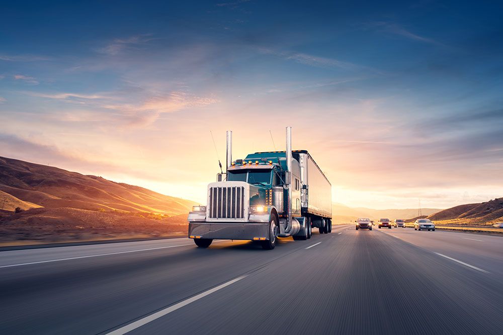 Powerful semi-truck driving on highway at sunset, with scenic mountains in the background.