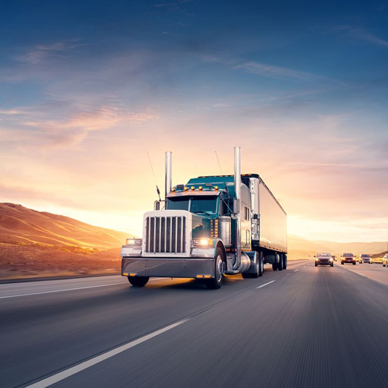 Powerful semi-truck driving on highway at sunset, with scenic mountains in the background.