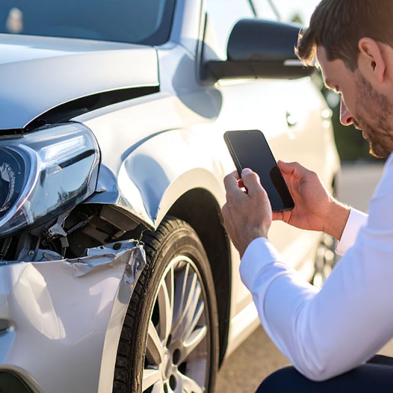 Man photographing car accident damage for insurance claim documentation.