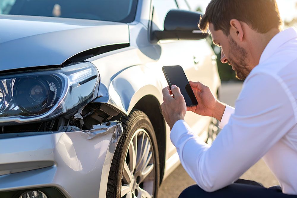 Man photographing car accident damage for insurance claim documentation.