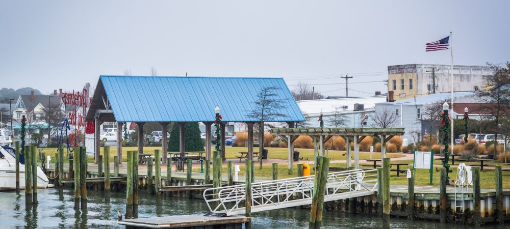 Harbor pier with blue-roofed building, American flag, and boats on a cloudy day.