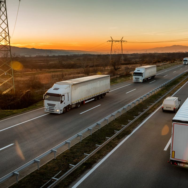 Convoys of White semi-trucks passing each other on a highway with a sunset and mountains in the background