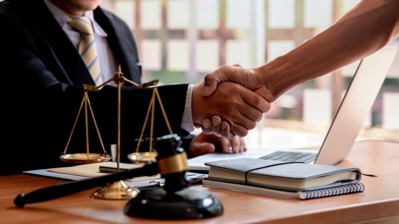 Handshake between lawyer and client at office desk with legal documents.