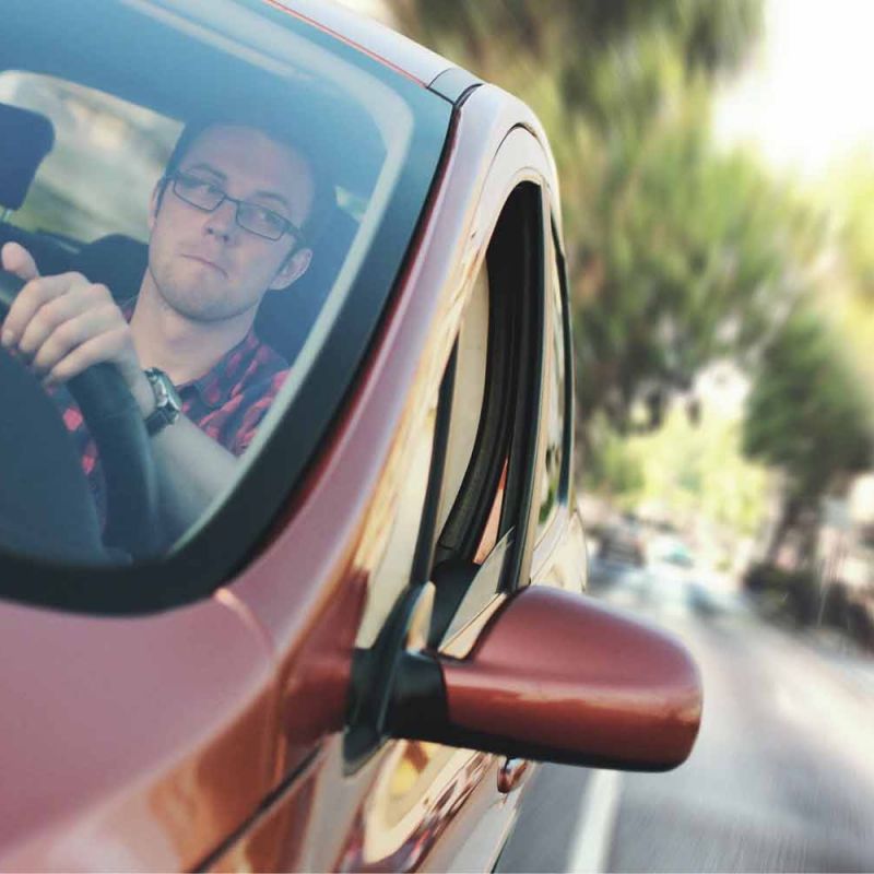 Man wearing glasses driving a red car