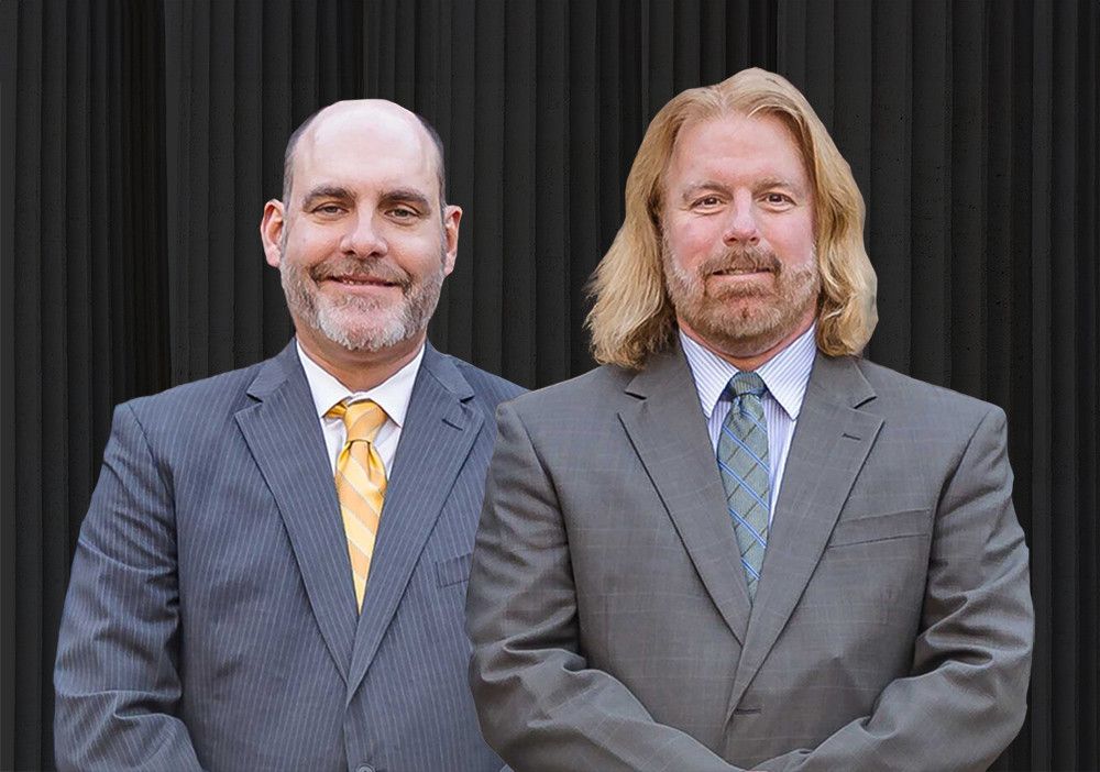 Two businessmen in suits stand together against a black background, smiling confidently.